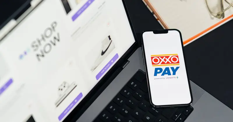 A mobile phone with OXXO Pay on a laptop used for online shopping.
