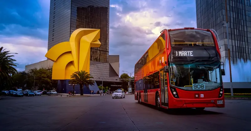 Red double decker bus in front of El Caballito sculpture, Mexico City, capturing urban transportation.