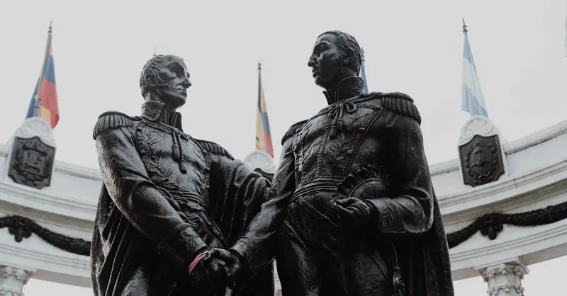 Historic statues at Hemicycle de la Rotonda, Guayaquil, Ecuador, captured with flags in the background.