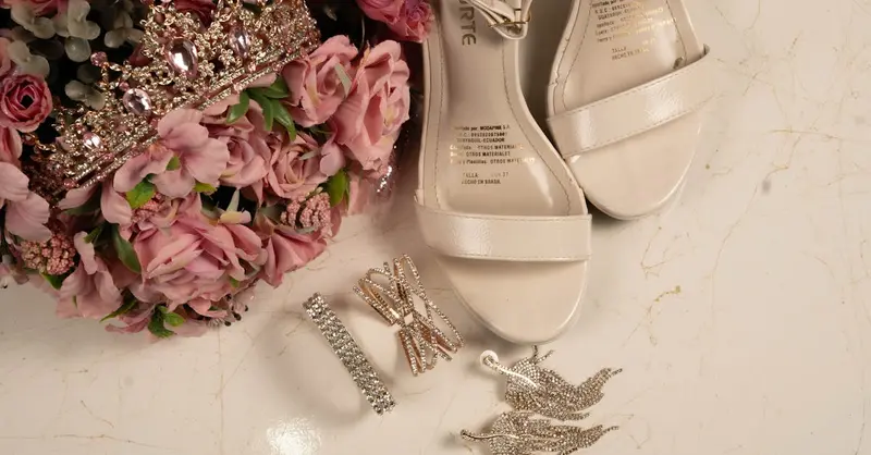 A flat lay of quinceañera accessories including shoes, tiara, and flowers on a marble surface.