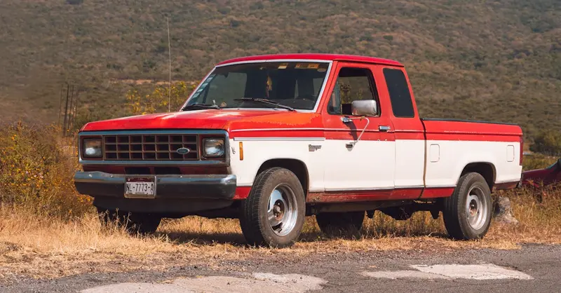 A vintage red and white pickup truck parked on a roadside in La Yerbabuena, Mexico.