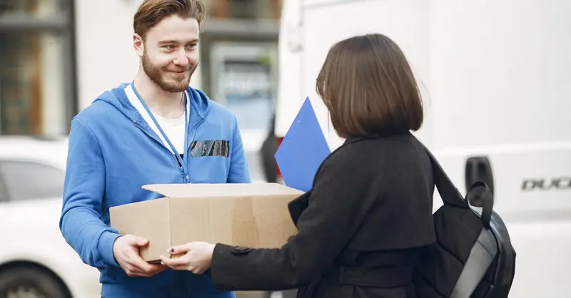 Candid moment of a deliveryman handing a package to a woman outside by a van.