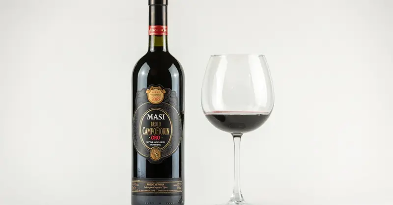 Red wine bottle and glass on a white background, showcasing Masi Brolo Campofiorin from Italy.