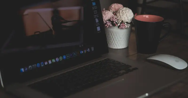 A cozy workspace featuring a laptop, coffee cup, and artificial flowers, ideal for remote work.