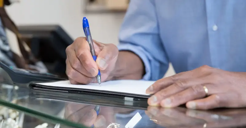 A person writing in a notebook at a glass counter, capturing business and office themes.