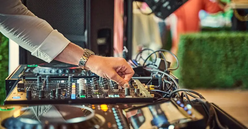 Close-up of DJ adjusting an audio mixer outdoors, showcasing modern music equipment.
