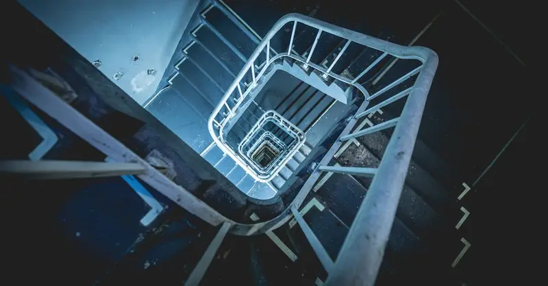 High-angle view of a spiral staircase with metal railings in a dark, dramatic setting.