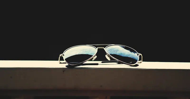 A close-up of aviator sunglasses reflecting the sky, set against a dark background.