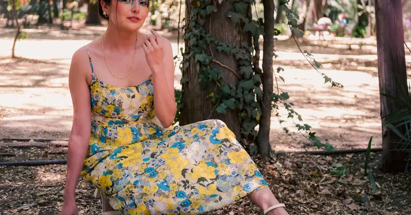 Stylish woman in floral dress poses in a lush park setting, embracing nature.