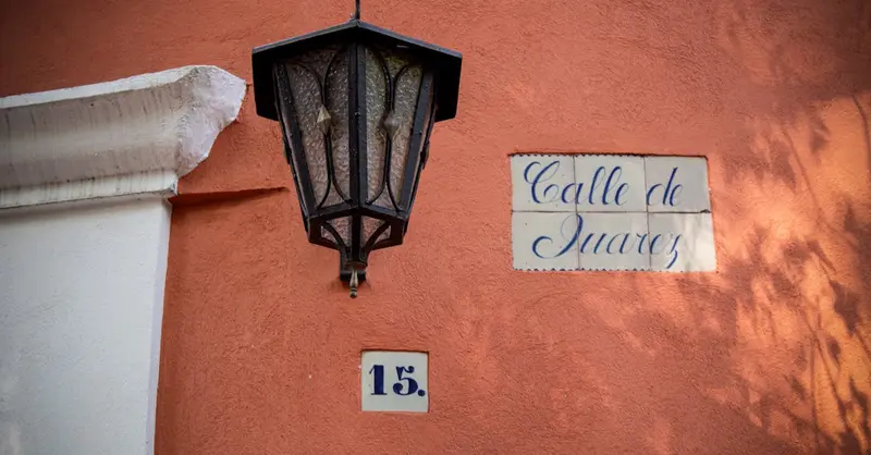 A street light casting shadows over a 'Calle de Juarez' sign and address number in Mexico City.