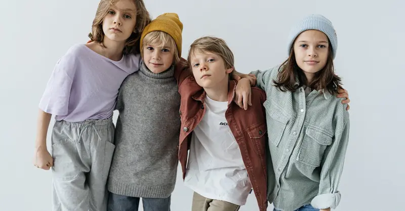 Group of fashionable kids posing in a studio setting wearing trendy outfits.