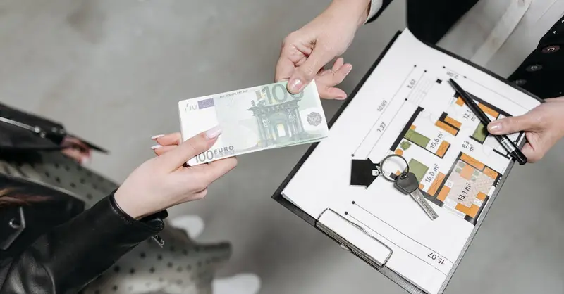 Close-up of a real estate transaction with euro bill, keys, and floor plan.
