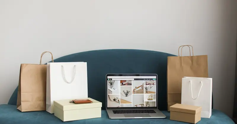 A laptop surrounded by shopping bags and boxes on a blue sofa, ideal for online shopping themes.