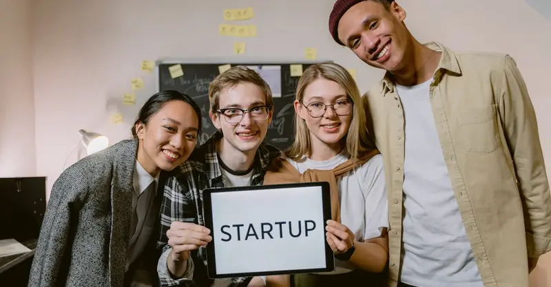 A diverse group of young professionals in a startup office, smiling and holding a sign.