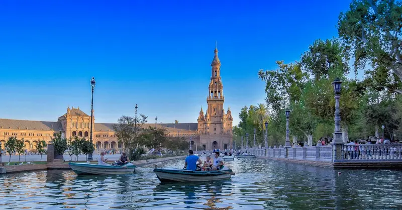 Colorful view of people boating in Plaza de España, Seville under a clear sky.