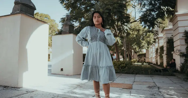 A woman in a traditional dress poses in a sunlit courtyard in San Cristóbal de las Casas, Mexico.