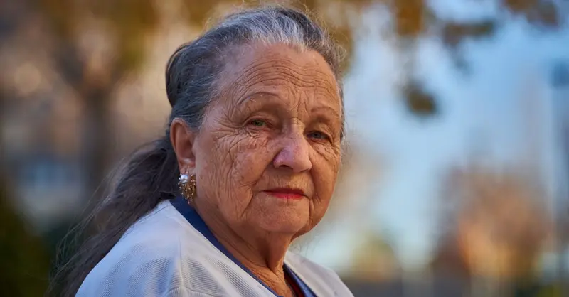 Senior woman with thoughtful expression in a sunny outdoor setting.