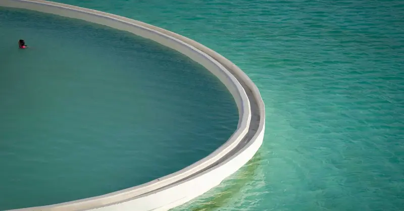 A person swims in a tranquil curved pool overlooking the turquoise ocean in La Serena, Chile.