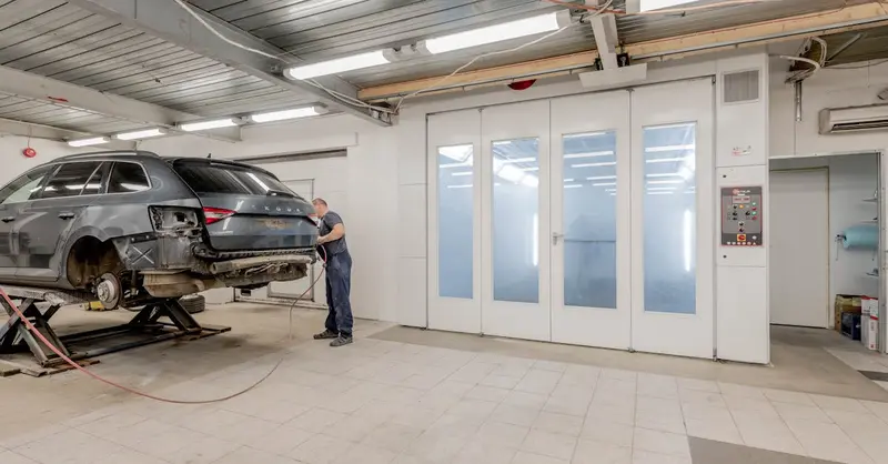 Mechanic repairing a car indoors at an auto workshop, focusing on vehicle maintenance.