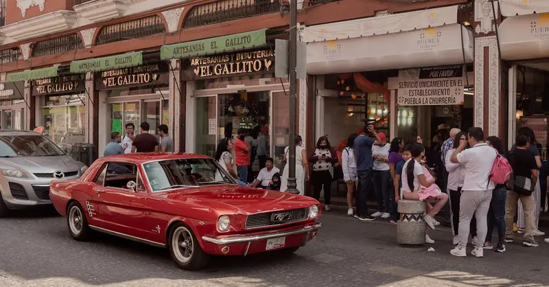 A vibrant red Ford Mustang on a bustling street in Heroica Puebla de Zaragoza, Mexico.