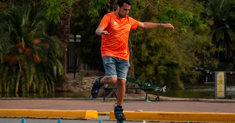 Man wearing an orange shirt roller skating through slalom cones outdoors, showcasing skill and balance.