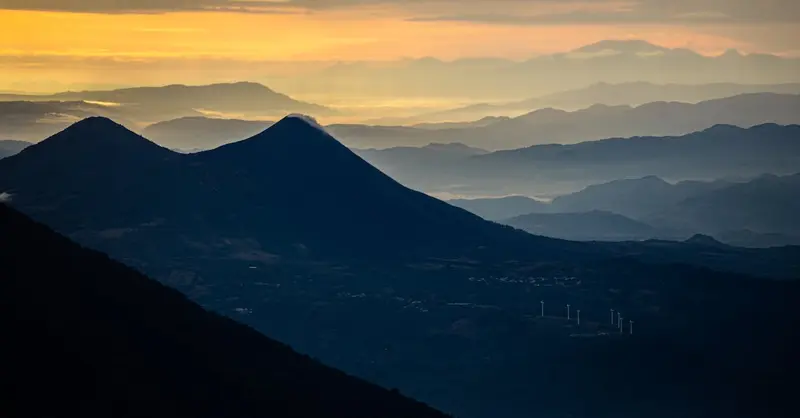 Dramatic aerial view of Guatemala's mountain ranges at sunrise with layered mist and warm hues.