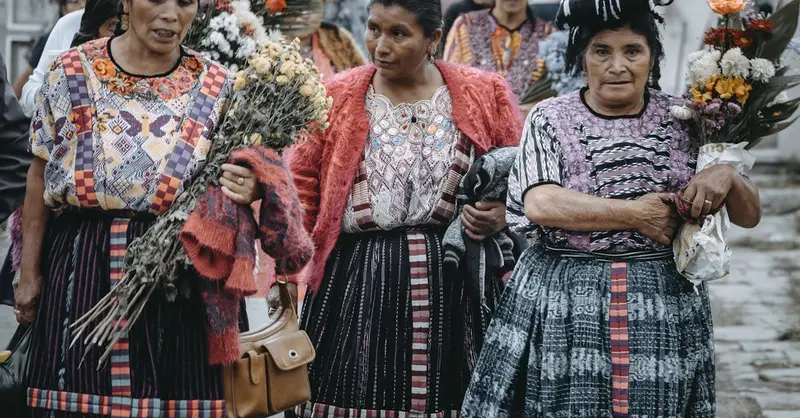 Women in traditional Guatemalan clothing gather with flowers, celebrating a cultural festival.