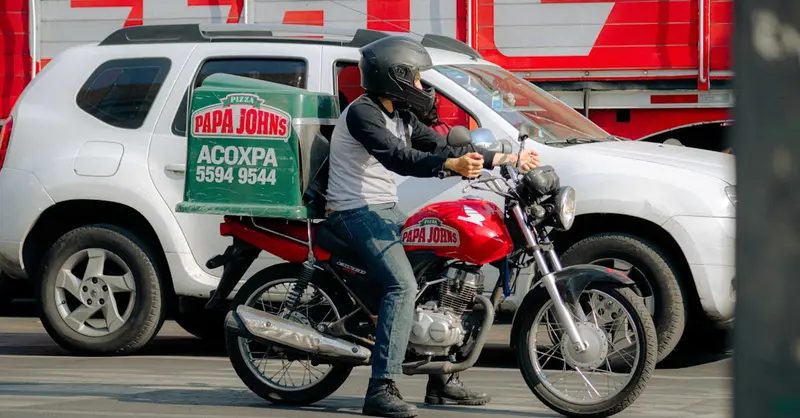 Pizza delivery rider on a motorcycle waits at a busy city street intersection.