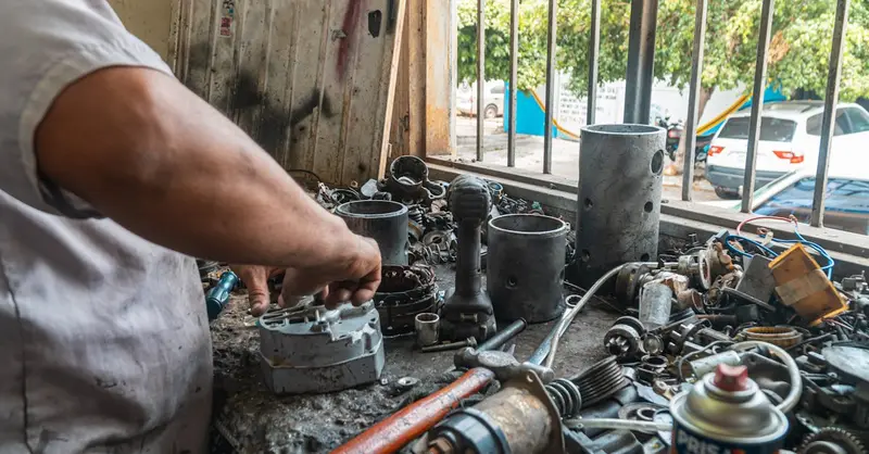 Mechanic organizing auto parts in a busy workshop, surrounded by tools and equipment.