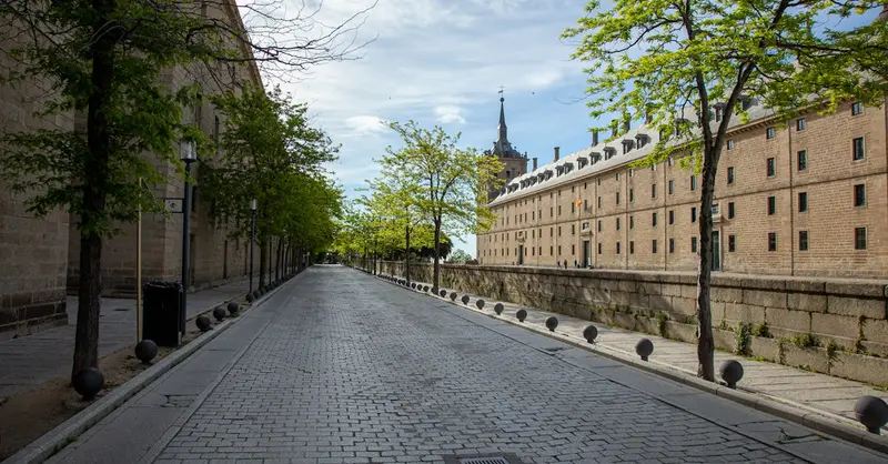 Empty street lined with trees and historic buildings at the Royal Site of San Lorenzo de El Escorial, Spain.