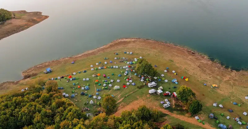 Aerial view of a vibrant lakeside campsite with numerous tents and scenic surroundings.