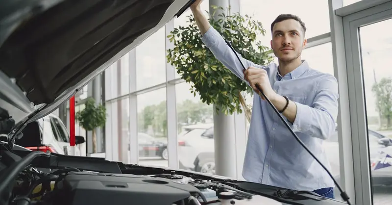 A man carefully checking a car engine in a bright, modern car showroom.