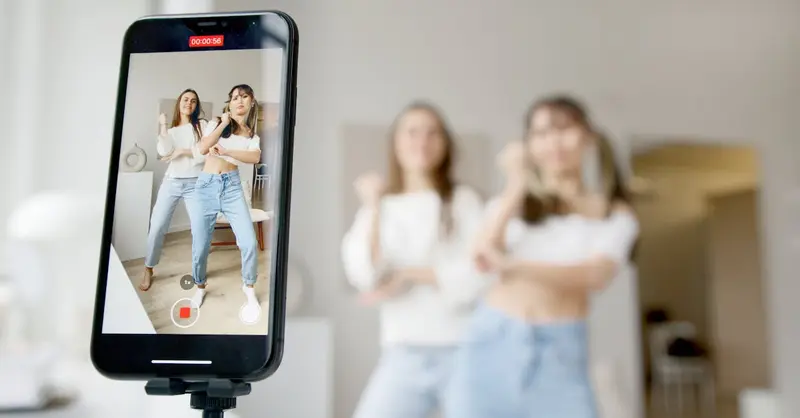 Two women dance in front of a smartphone camera, recording content indoors.