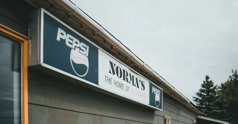 Photo of Norma's Restaurant exterior featuring a vintage Pepsi sign on a cloudy day.