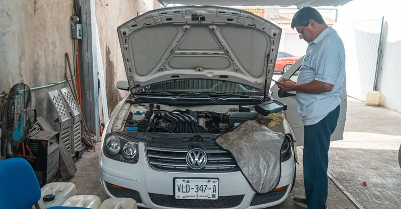 A mechanic examines a Volkswagen engine in a garage setting, focusing on car maintenance.
