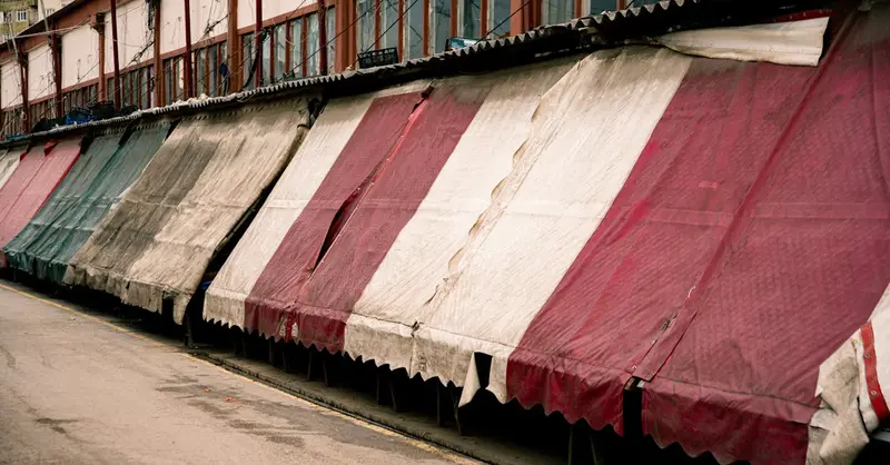Row of closed market stalls with colorful striped awnings in an empty street.