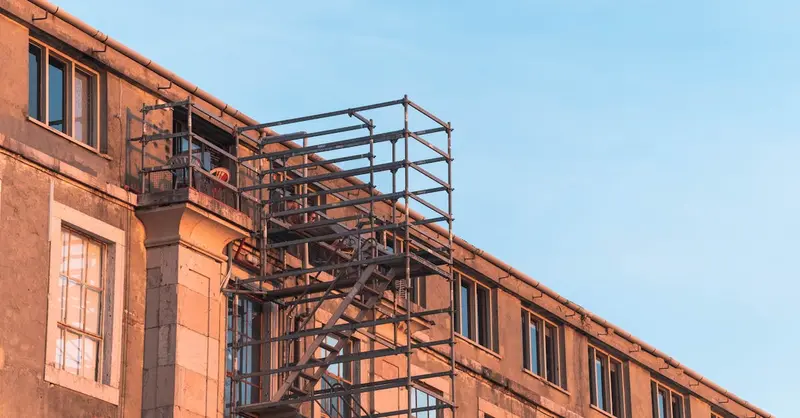 Residential building facade in Lisbon with scaffolding and fire escape under clear sky.