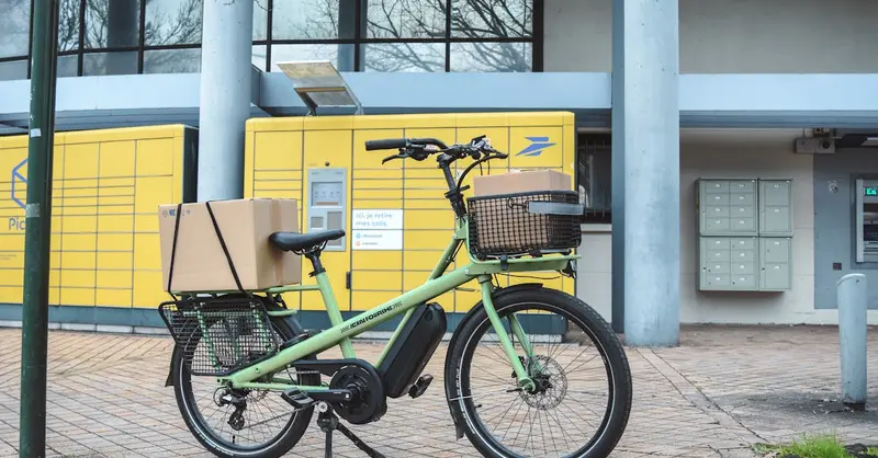 Green electric cargo bike with parcels at La Poste in France, showcasing urban delivery solutions.