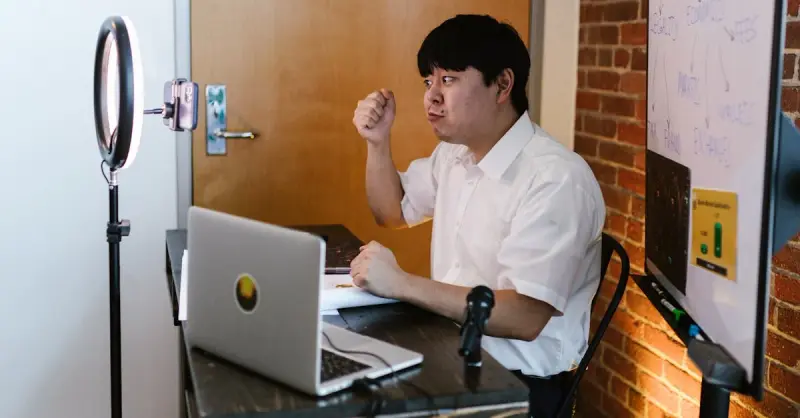 Asian man in white shirt conducts an online meeting with a laptop and ring light.