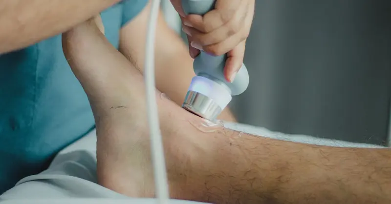 Professional physiotherapist using ultrasound device for leg treatment.