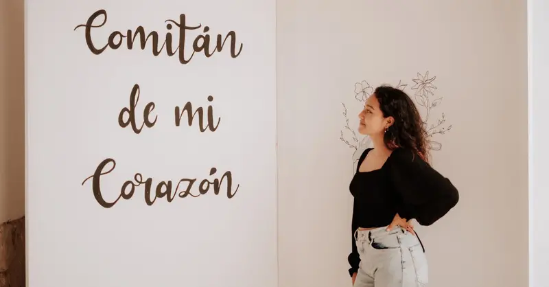 A woman in a black top and denim jeans admires a wall with 'Comitán de mi Corazón' text.