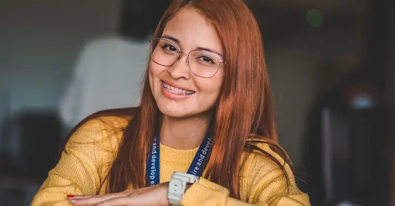 Portrait of a red-haired woman wearing glasses, smiling indoors.