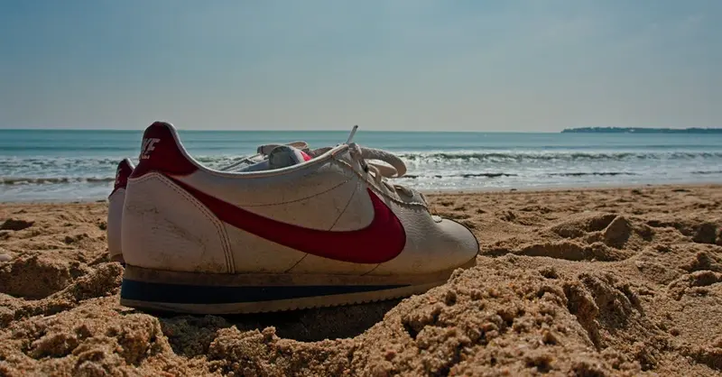A single sneaker on the sandy beach of La Baule, France, with ocean waves in the background.