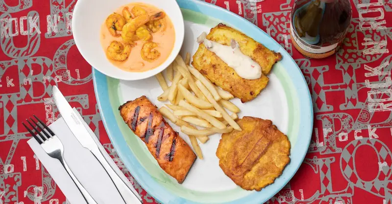 Delicious Colombian seafood platter featuring shrimp, fried plantains, and fish with a creamy sauce.