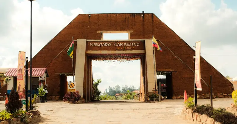 Rustic entrance of Mercado Campesino with flags, capturing a sunny marketplace scene.