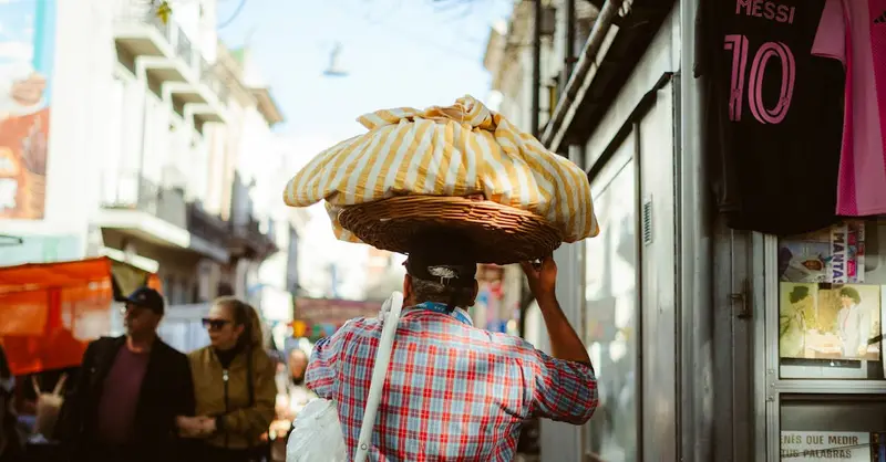 A bustling Buenos Aires street vendor carries goods through a lively market scene.