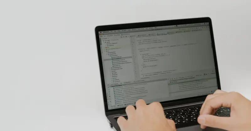 Hands typing code on a laptop in a workspace. Indoor setting focused on software development.