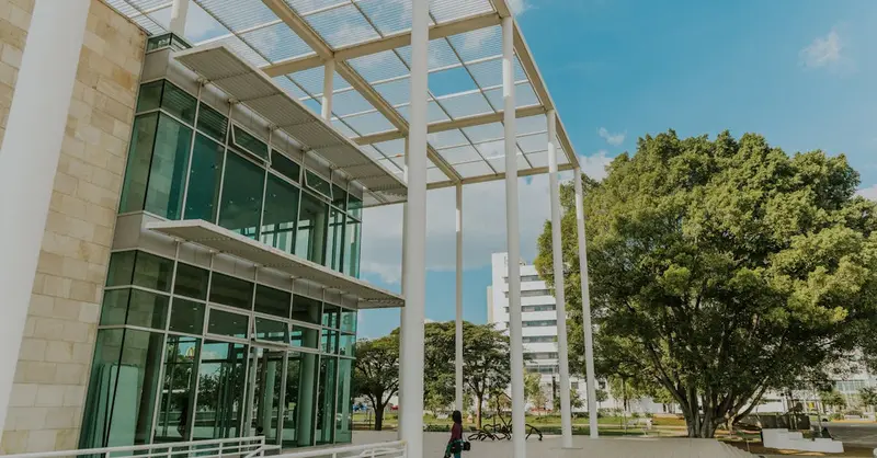 A modern building with glass windows surrounded by trees under a clear blue sky.