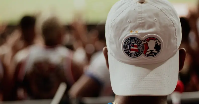 A dedicated football fan sport ing an Esporte Clube Bahia cap watches the game.