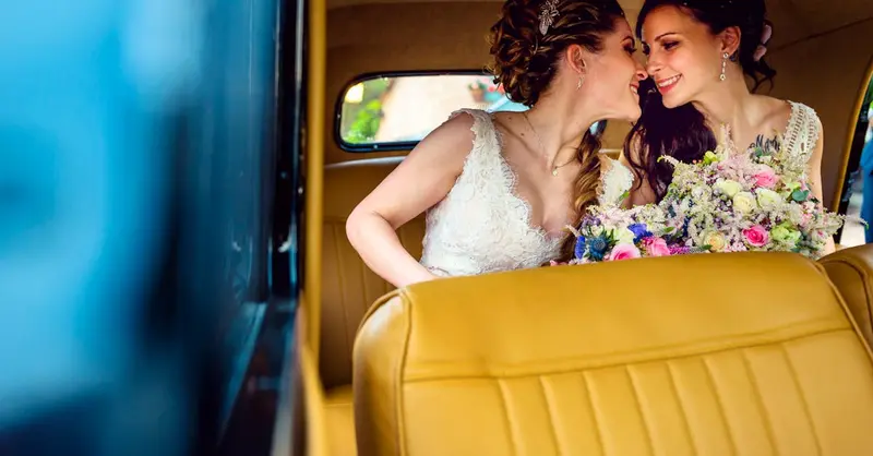 Joyful same-sex couple sharing a moment in a vintage car on their wedding day.